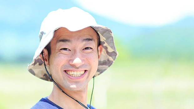 山をバックに帽子を被っている笑顔の天野琢也さんの顔をアップで写した写真