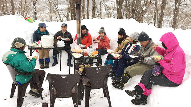 雪を椅子のように形どり、そこに座りながら食事をしている茅ボッチの会の方々の写真