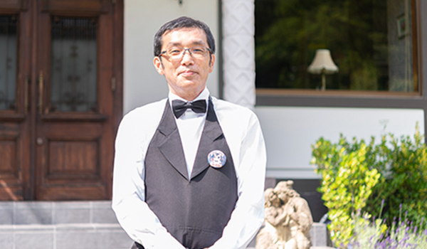 白いシャツに黒い蝶ネクタイ、ベストを着た小川文男さんを正面から写した写真