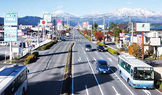 右側が3車線、左側が2車線の道路の両側にたくさん店舗が並んでいる街並みの写真