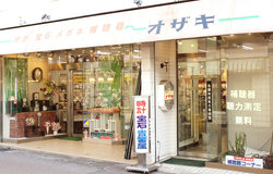 「オザキ」と店舗入口上部に書かれ、入口には時計・宝石・貴金属と書かれた看板が置かれている尾崎時計店の入口を写した写真