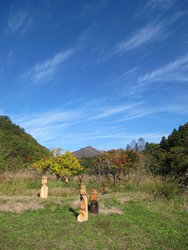 奥に山が見える晴天の屋外に、ふくろうの木彫りが並べられているロッヂ古代村の写真