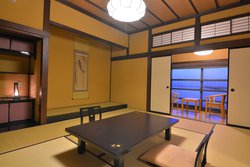 窓際と室内に椅子とテーブルがあり、床の間に掛け軸などがある純和風の室内の写真