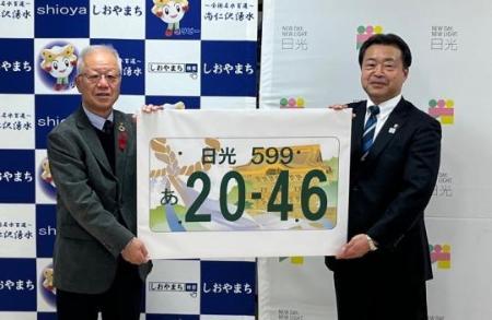 日光ナンバープレートのデザイン案の最優秀賞を手に持つ日光市長と塩谷町長