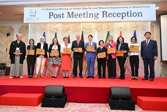 「Post Meeting Reception」と書かれたボードの前で関係者の方々が横1列に並び記念撮影をしている写真