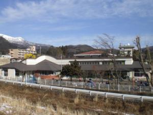 奥に雪が積もった山脈があり、横長で白とグレーを基調とした日光保育園園舎の写真