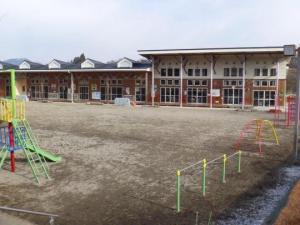 園庭にカラフルな滑り台が設置され、白と茶色を基調とした2階建ての落合児童館館舎の写真