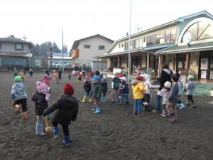 園庭で防寒着を着たたくさんの子どもたちが遊んでいる写真