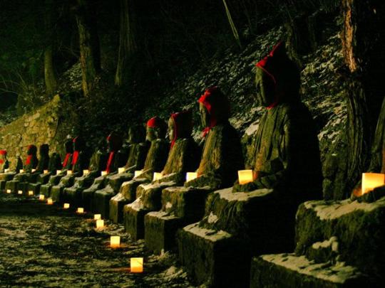一列に並んだ化け地蔵(並び地蔵)が赤い頭巾をかぶり、前にはとうろうが置かれている写真
