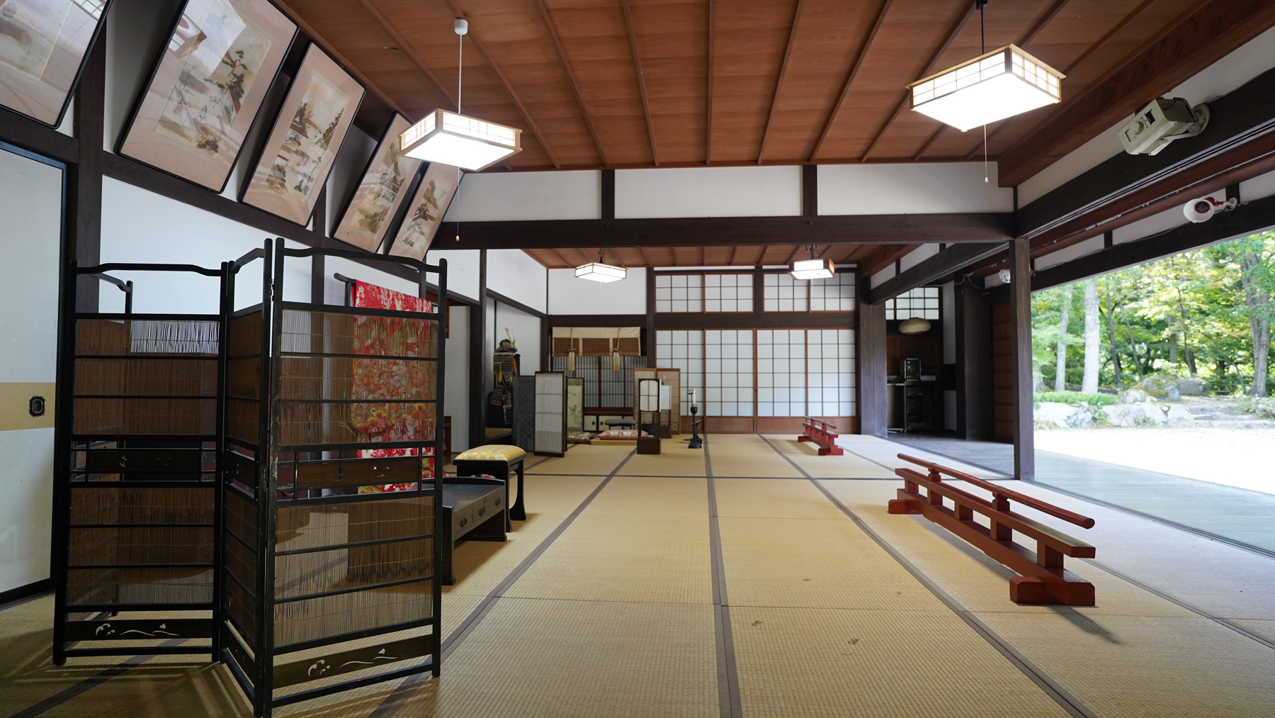 扉が全て取り除かれた室内に赤い着物や絵画などが展示されている和室を写した写真