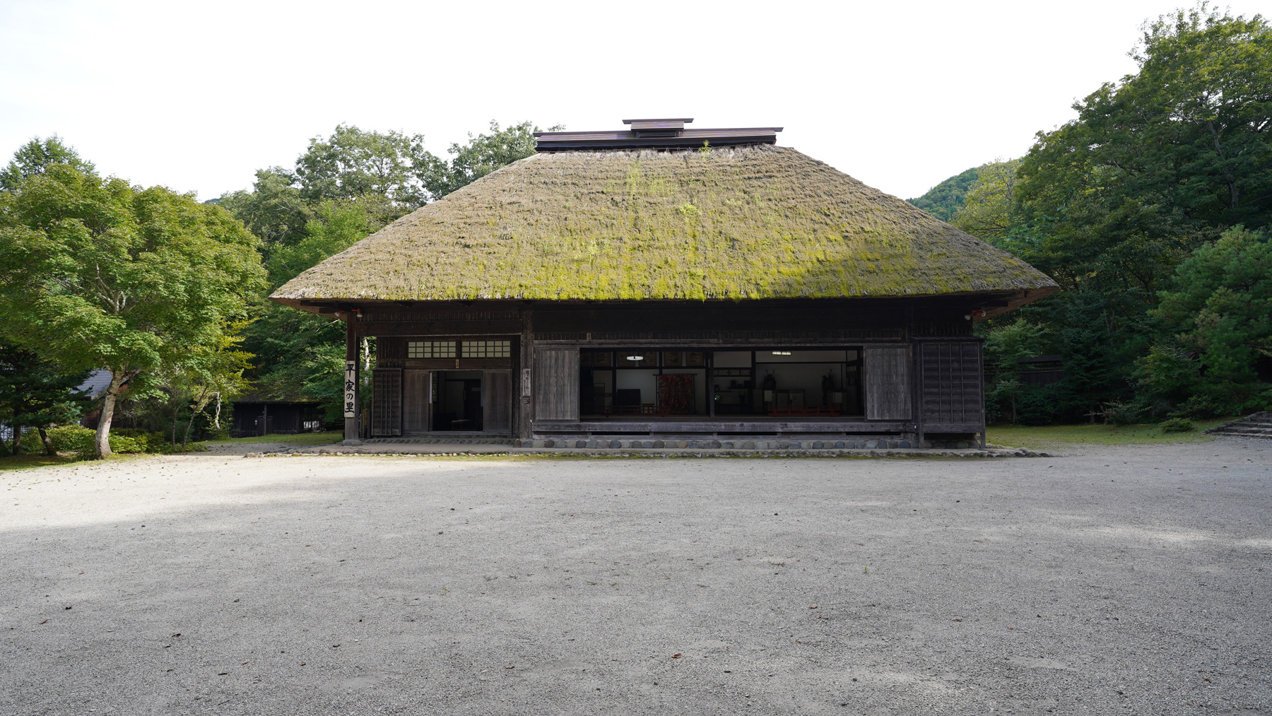 広い敷地にぽつんと建つ茅葺屋根をした平家の里の建物を正面から写した写真