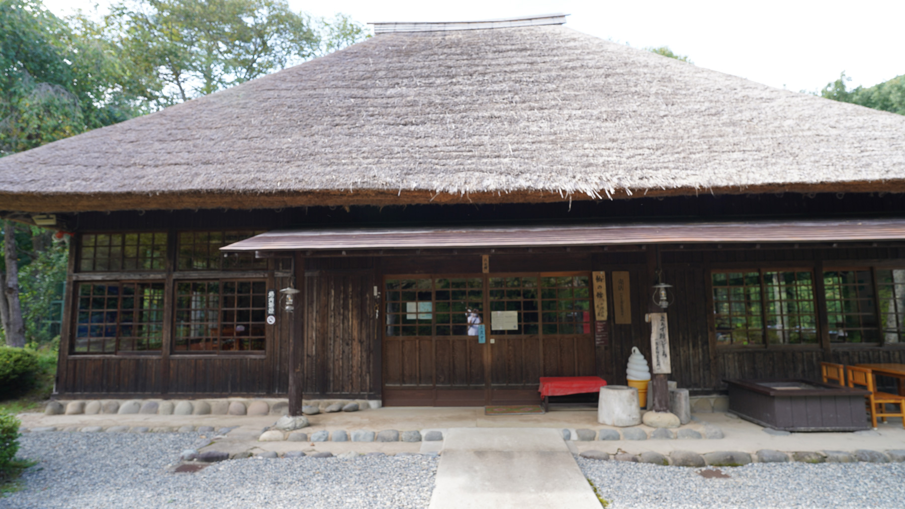 茅葺屋根の家屋の入り口にソフトクリームの形をした置物や休憩できるスペースがあるお休みどころを写した写真