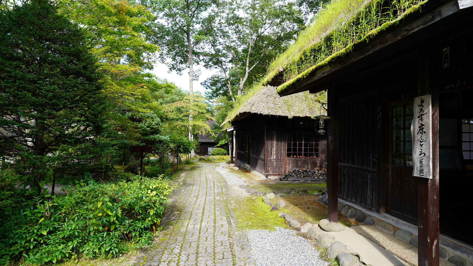 柱に「よろず床しどころ(展示館)」と書かれた案内板があり、通理を中心に右横に3棟の建物が並んでいる写真