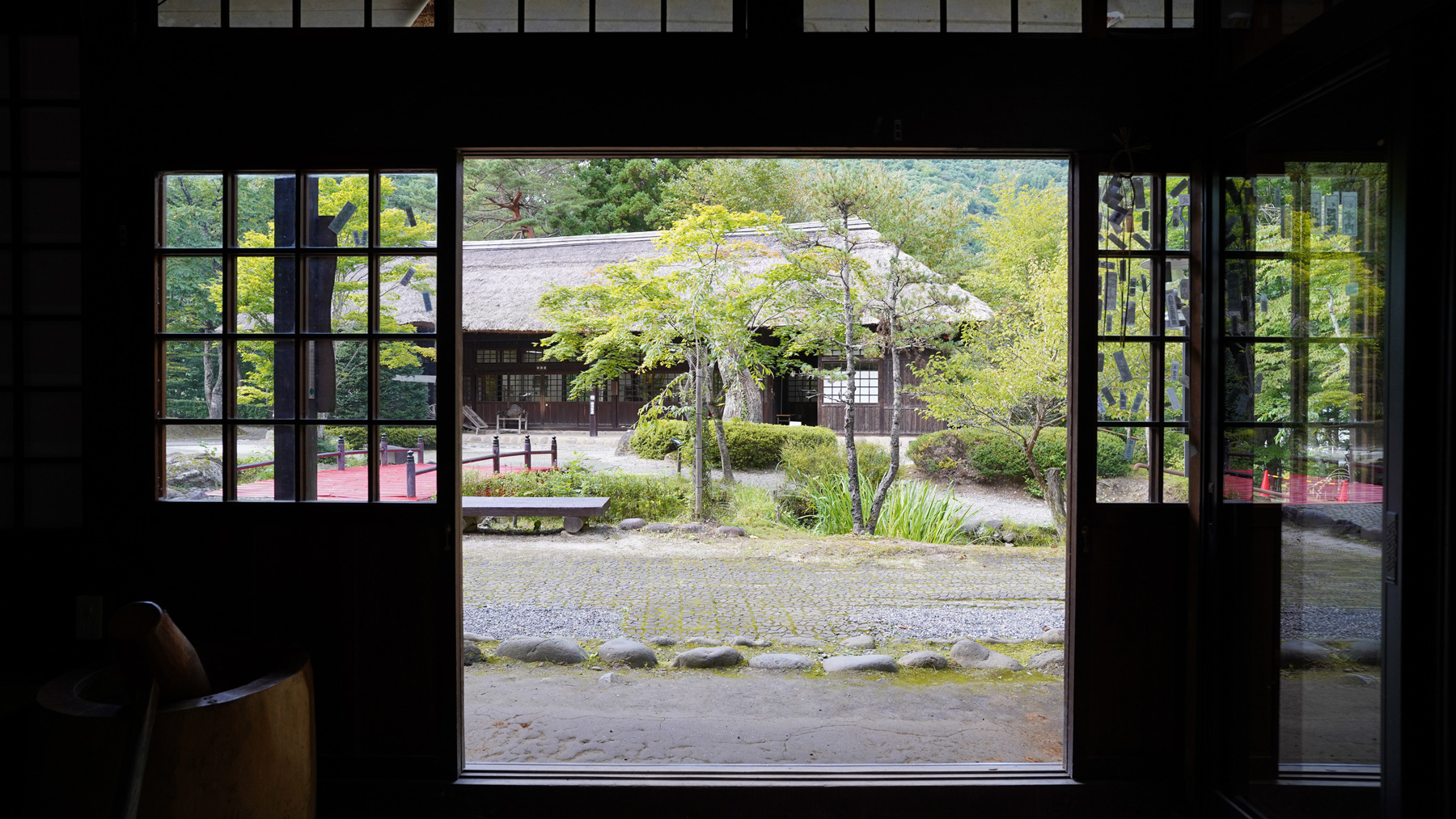 扉を開いた奥に見える茅葺屋根の家屋と庭園の写真