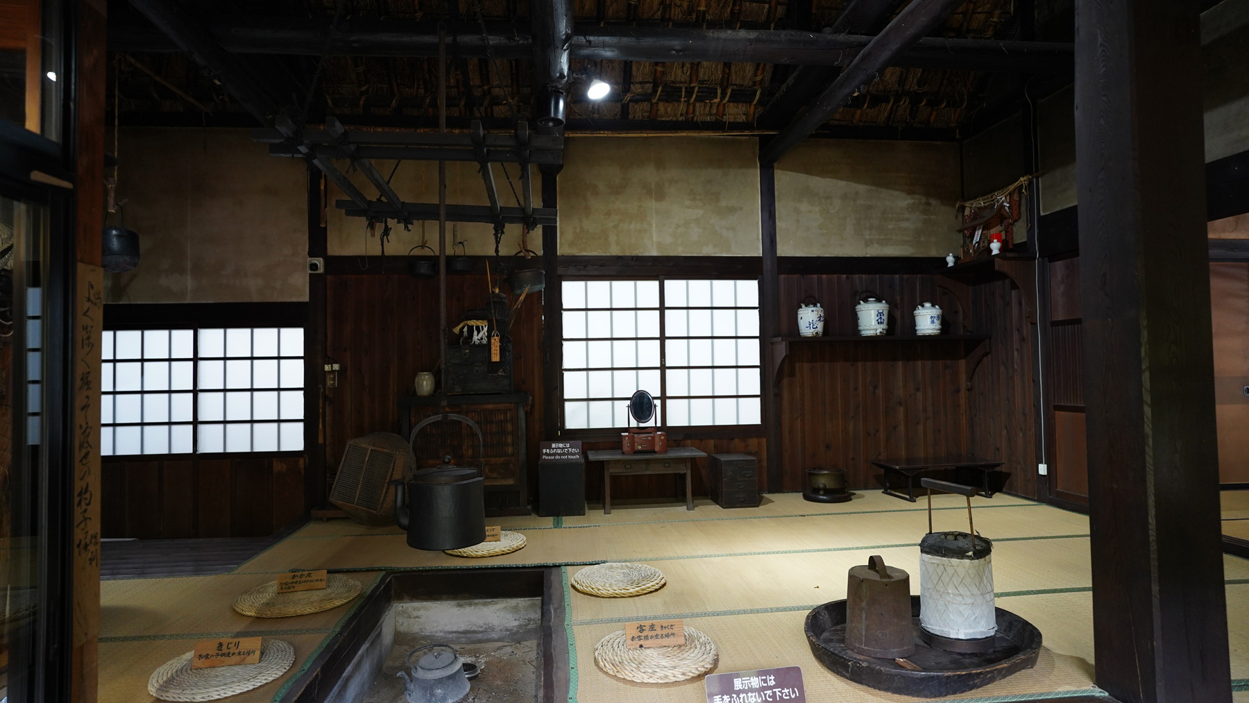畳張りの部屋に囲炉裏があり昔の様々な道具が展示されている室内を写した写真