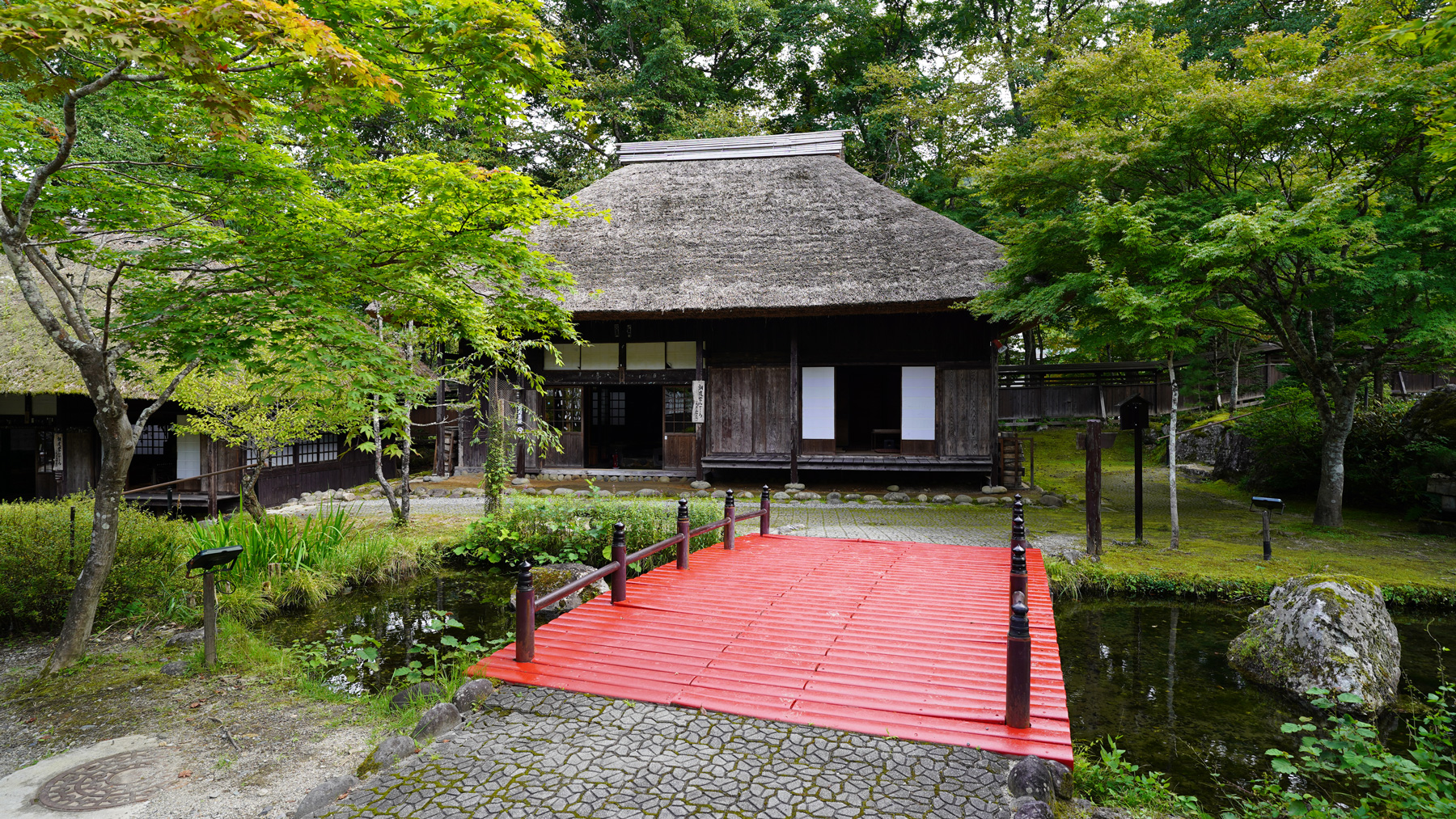 床板が赤い橋を渡った先に見える茅葺屋根の平家の里の写真