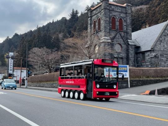 背景にレンガ造りの灰色の建物がある道路を走行する赤い観光バスの写真