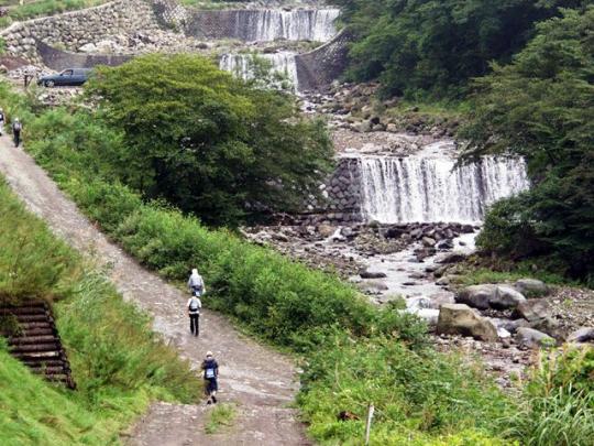 稲荷川砂防堰提群が右手にあり、左の道を数名の人が歩いている写真