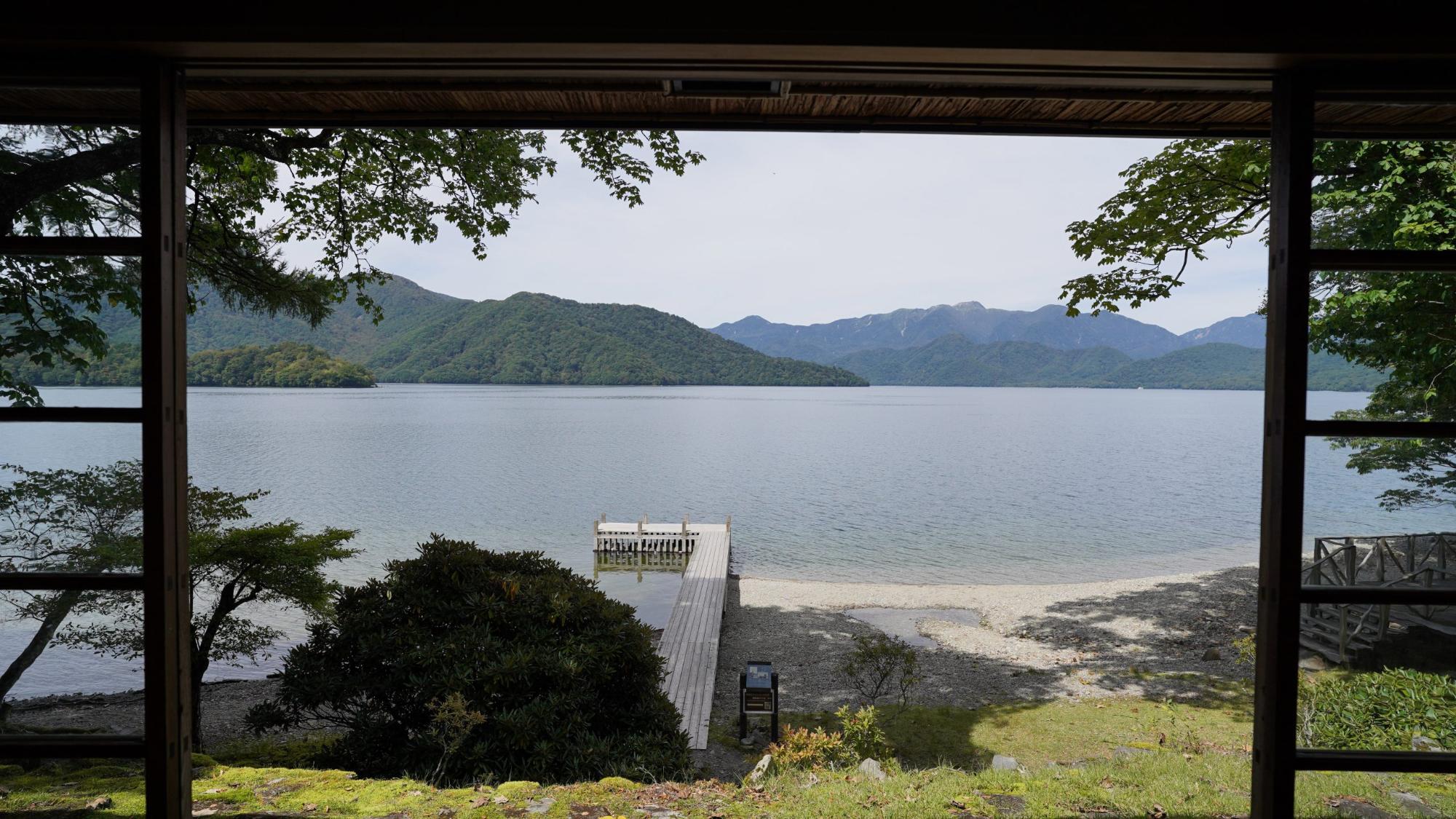 奥には山、手前に湖と桟橋が見えている室内の大きな窓辺からの写真