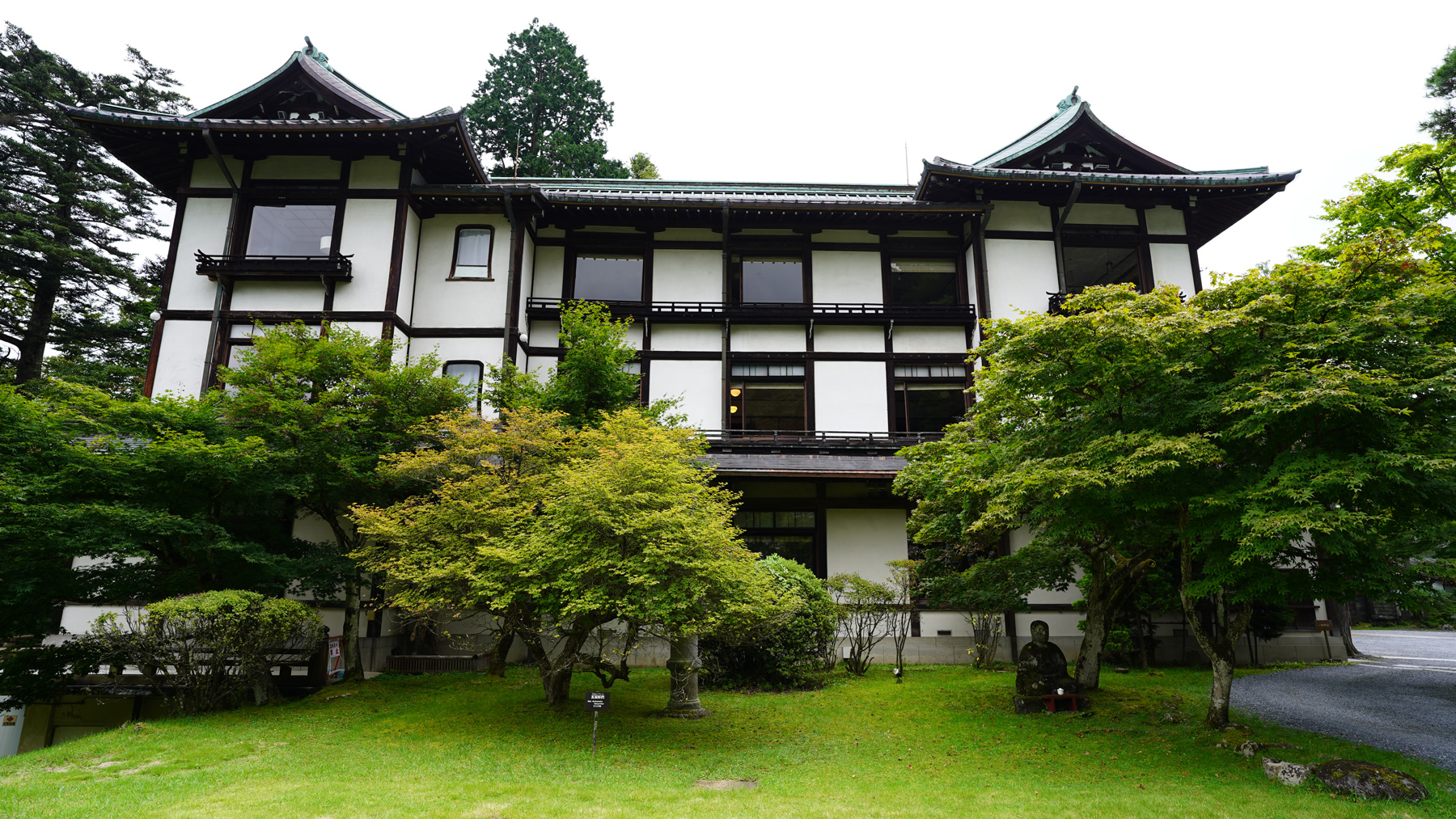 緑の庭園の奥に建つクリーム色の外壁に茶色の枠がアクセントになっている建物の写真