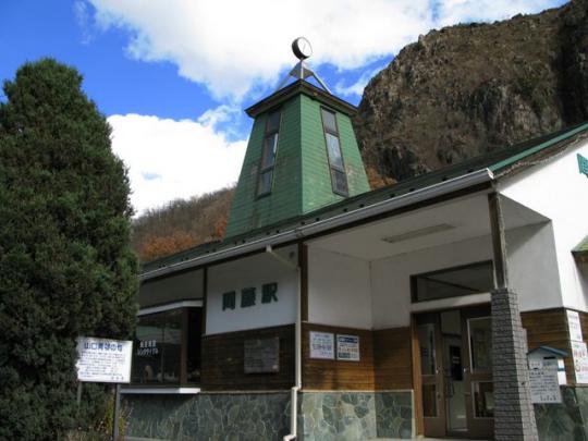 山を背景に間藤駅の駅舎を斜めから撮った写真
