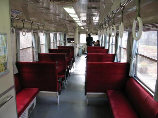 電車内に赤い乗車席があり、運転手と客が乗っている写真