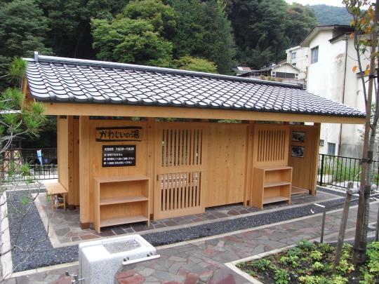 瓦屋根の建物の外壁にに「かわじいの湯」と書かれた木製の看板が設置してある足湯の写真