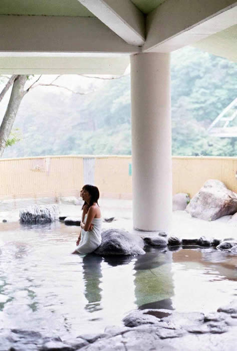 露天風呂「薬師の湯」に足だけ浸かり、石に腰をかけている2人の女性の写真