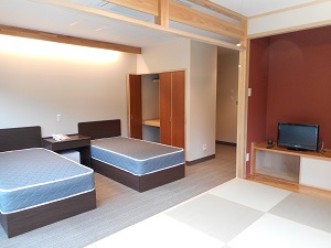 手前の座敷にテレビが置いてあり、後方が洋室で2台のベットが置かれてある客室内の写真