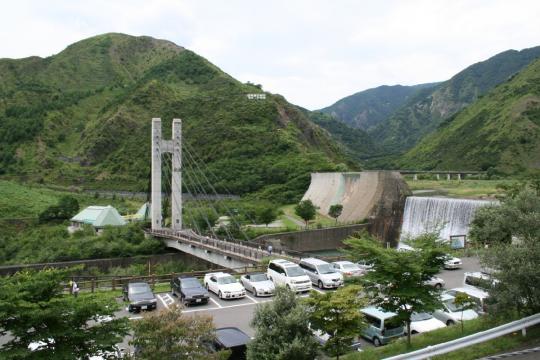 山々に囲まれ、足尾ダムと公園駐車場をつなぐ銅橋がある銅親水公園を高い場所から撮影した写真
