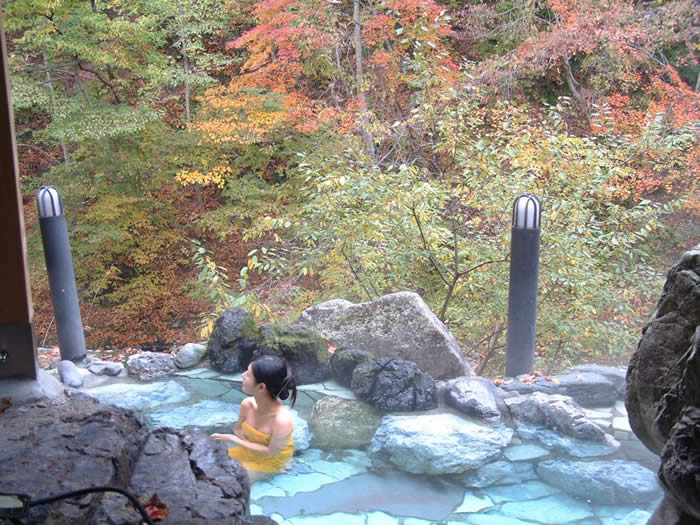 紅葉した木々に囲まれながら温泉に入っている女性の写真