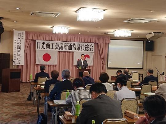 演壇で市長が話をするのを座って聞いている参加者の人たちの後方から写した総会の様子の写真