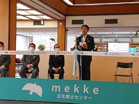 下に「mekke日光郷土センター」と書かれたパネルが置かれ、市長が挨拶をしているmekke日光郷土センターリニューアルオープンセレモニーの様子の写真