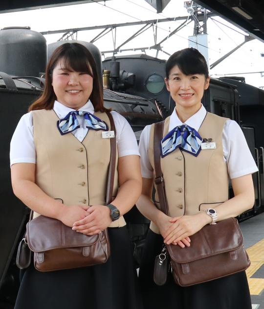 首元に水色のリボンが付いた制服を着たSLアテンダントの中島美樹さん井池忍さんが笑顔で並んでいる写真