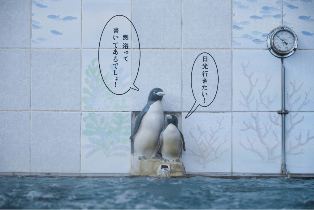 温泉のお湯の吹き出し口の上でお母さんペンギンが「黙浴って書いてあるでしょ!」子供ペンギンが「日光いきたい!」と言っているペンギン親子の人形の写真