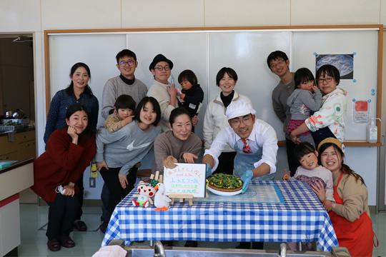 青と白のチェック柄のテーブルクロスの上に料理が置かれ、モグローカルのイベントに参加された方の集合写真