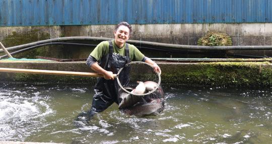 沢山のマスが入った玉網を持った、笑顔の神山勇人さんの写真