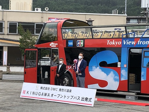 屋根の一部を取り払ったオープンカーのオープントップバス出発式であいさつをしている市長の写真