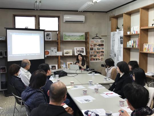 プロジェクタを使って説明する女性と、熱心に聞き入る参加者たちの写真