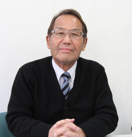こちらに笑顔を向けるメガネをかけた島田忠彦氏の写真