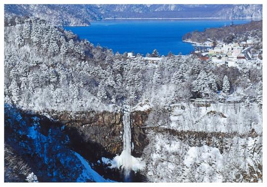 湖の手前の白銀の絶壁から流れ落ちる華厳の滝の写真