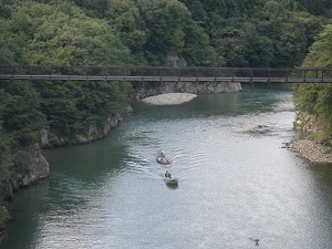 吊橋の下の川で数人の人々がボートに乗っている写真