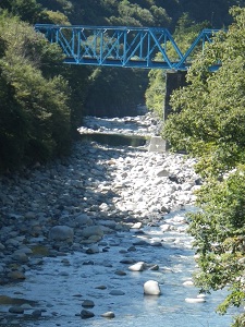 緑の山々に囲まれた青い橋とその下を流れる川の写真
