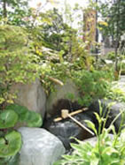 草木に囲まれ岩で造られた水場に柄杓が置かれている「いまいちの水」の写真