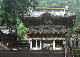 緑の木々の中に尊厳に建つ全体が黒塗りで金があしらわれた日光の社寺を正面から写した写真
