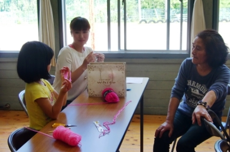 二人の女性があやとりをする女の子を見ている写真