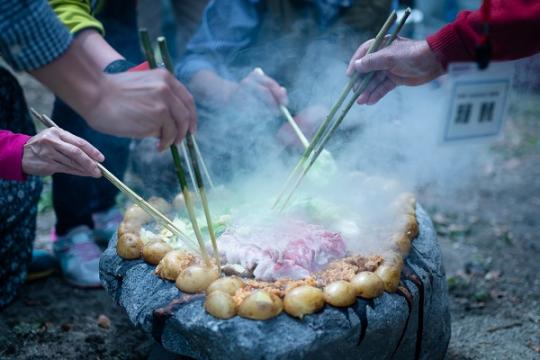 5人の参加者の方々が、手作りの箸でお肉や野菜を焼いている石焼きの様子写真