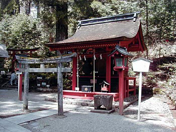 小さな鳥居の奥に建っている、入母屋造り、全体が朱色、黒い賽銭箱が設置されている二荒山神社末社朋友神社本殿の写真