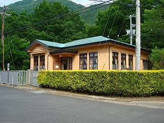 建物周りがフェンスと垣根で囲まれ、緑色の屋根、ベージュ色の外壁をした旧足尾銅山電話交換所の写真