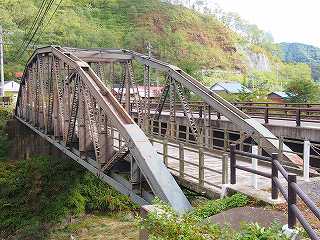 奥に山が見える手前に設置されているアーチ状の古河橋の写真